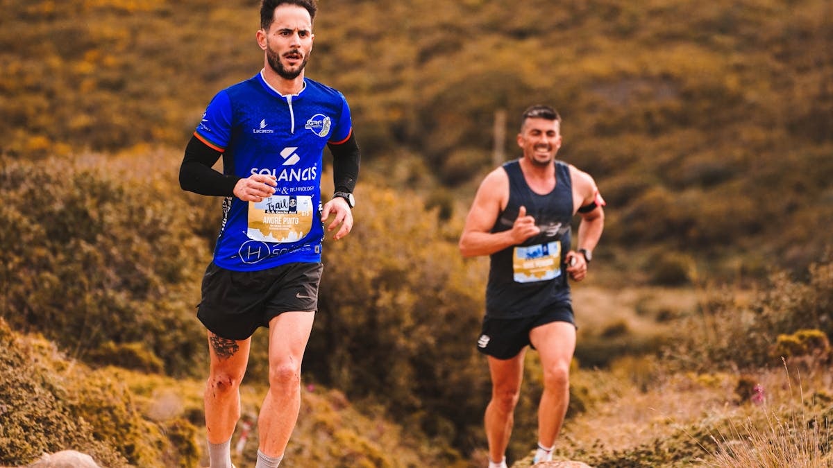 Dynamic image of two men trail running through an outdoor natural setting, showcasing energy and fitness.
